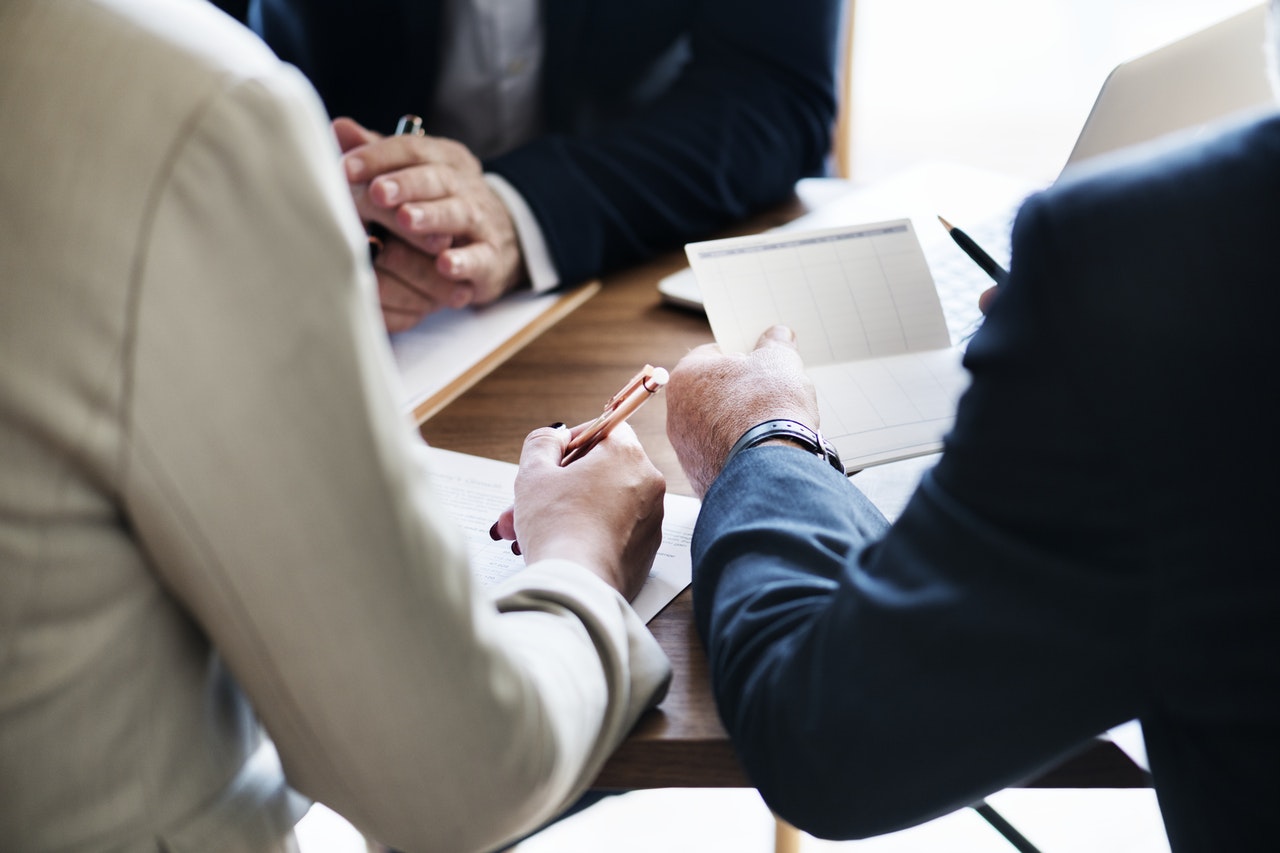 Three people reviewing and signing documents across a conference table